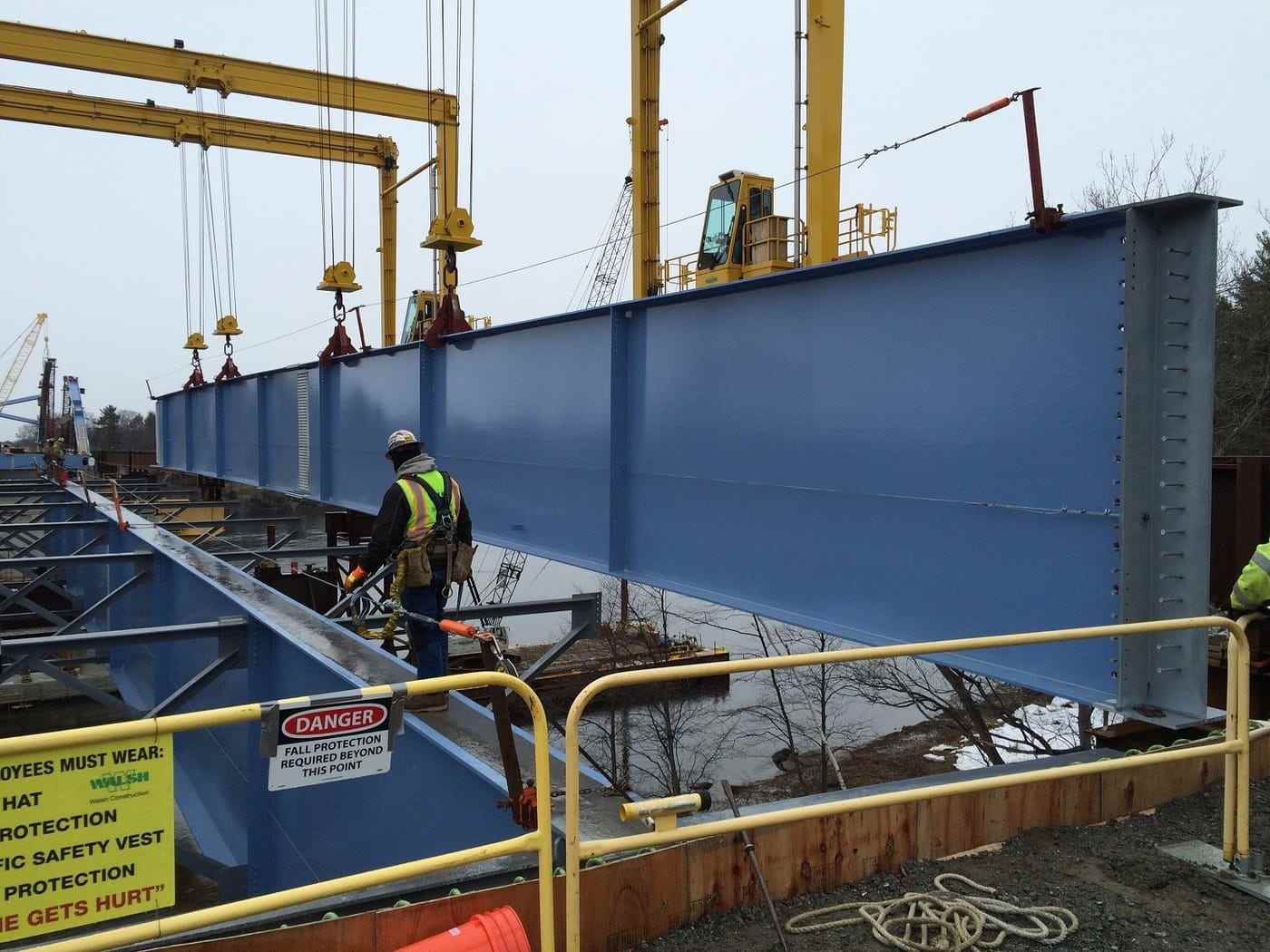 A fabricator working on a painted plate girder under an overhead gantry crane